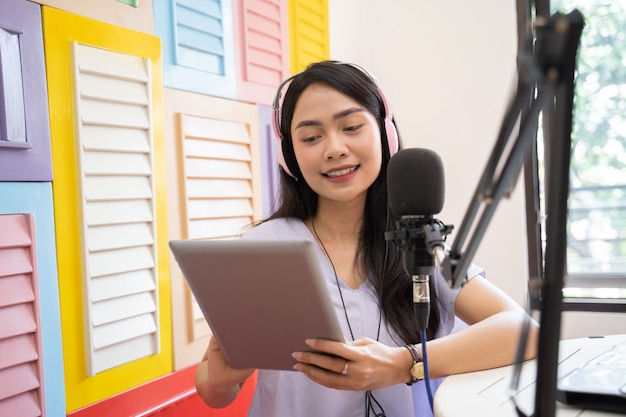 Una niña leyendo usando una tableta y usando audífonos hablando por un micrófono durante un podcast