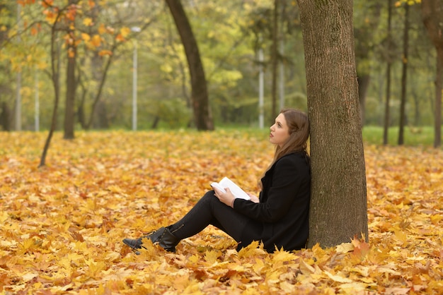 La niña con el libro en el bosque de otoño.