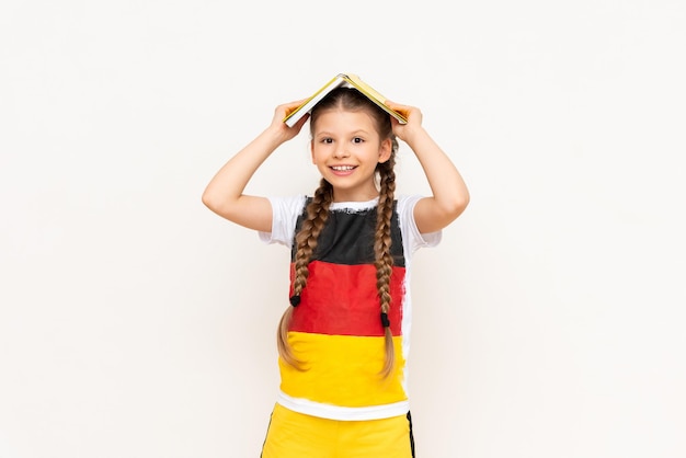 Una niña con un libro en la cabeza sobre un fondo blanco aislado Aprender alemán en los grados inferiores Un niño en una camiseta con la bandera de Alemania