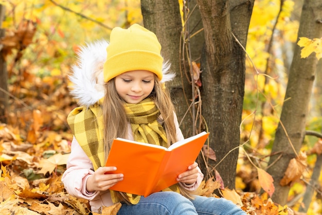 Una niña con un libro sobre las hojas de otoño.