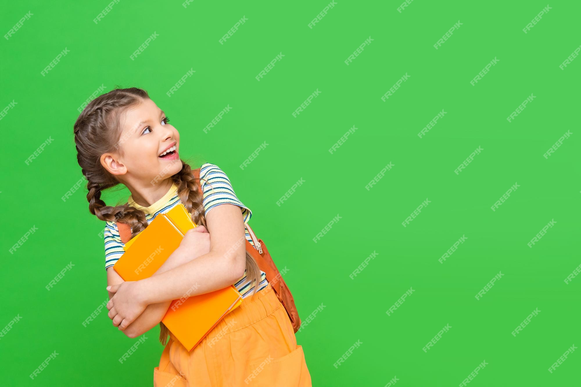 Una niña con libros de y un maletín escolar mira hacia otro lado muy feliz. niño sobre un fondo verde aislado con una copia del | Foto Premium