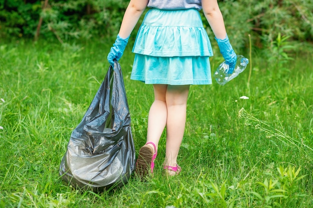 Niña limpia basura plástica en la hierba verde en el parque