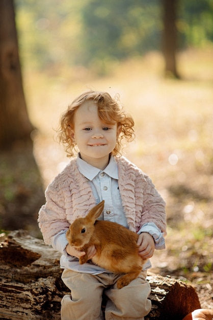 Niña linda de 3 años jugando con un conejo en el bosque de otoño