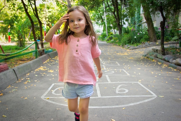 Niña linda de 4 años jugando a la rayuela en el patio de recreo al aire libre Enfoque suave selectivo