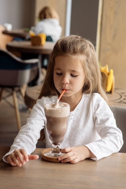 Niña linda de 5 años bebe cacao en un café