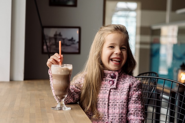 Niña linda de 5 años bebe cacao en un café