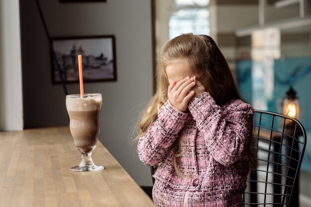 Niña linda de 5 años bebe cacao en un café