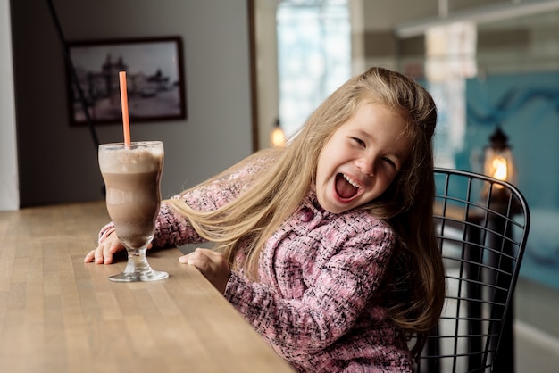 Niña linda de 5 años bebe cacao en un café