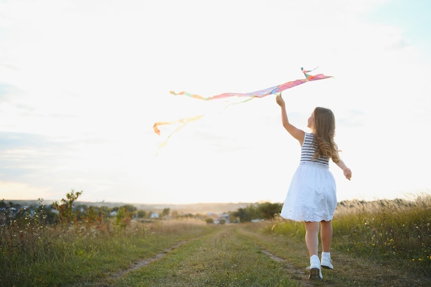 Niña linda de 7 años corriendo en el campo con cometa en el día de verano