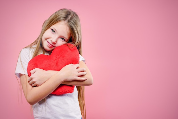 La niña linda abraza fuertemente el corazón grande del juguete rojo