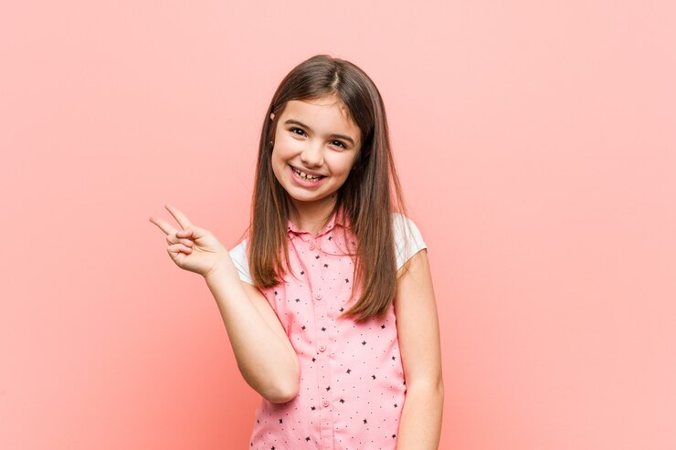 Foto niña linda alegre y despreocupada que muestra un signo de la paz con los dedos.
