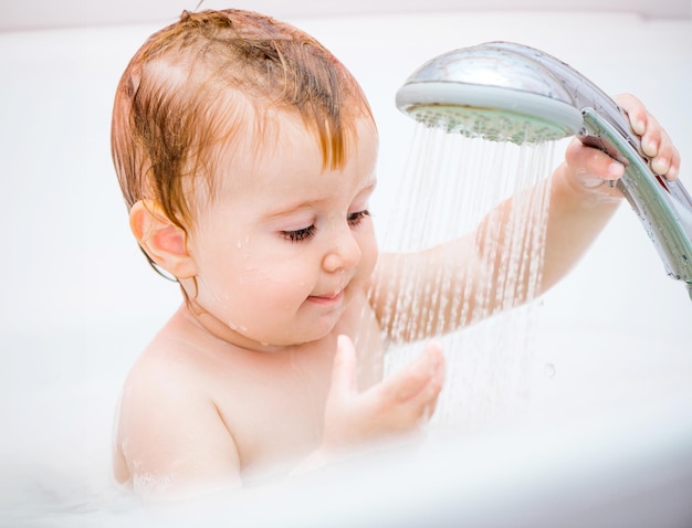 Una niña linda de un año se baña en una ducha.