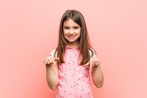 Foto niña linda apunta hacia abajo con los dedos, sentimiento positivo.