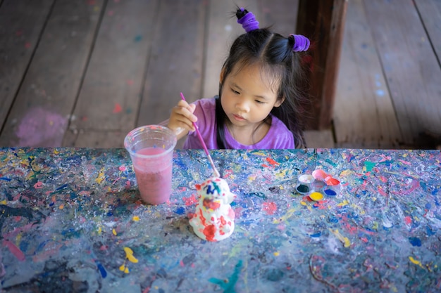 Niña linda asiática que se divierte pintar en la muñeca del estuco