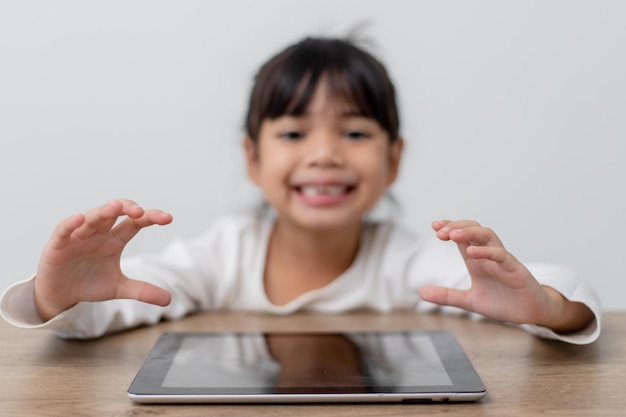 Niña linda asiática tocando la pantalla de la tableta digital en la mesa