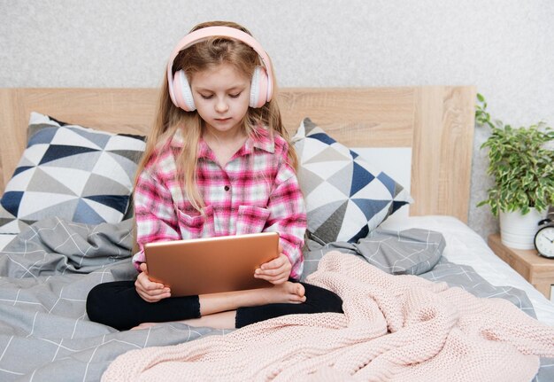 Una niña linda con auriculares está usando una tableta en casa