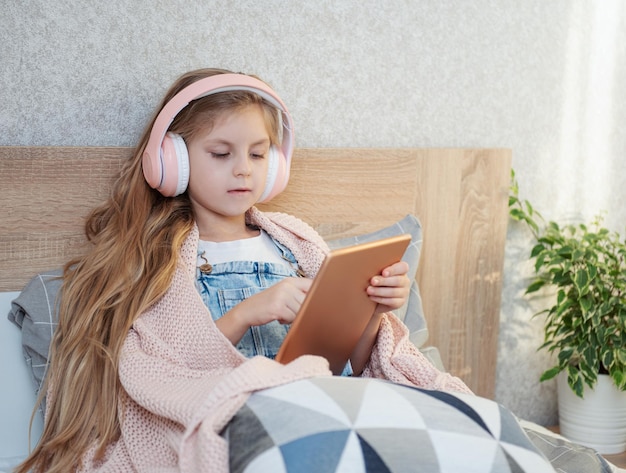 Una niña linda con auriculares está usando una tableta en casa