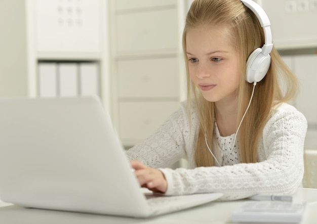 Niña linda en auriculares con portátil y lápiz en casa