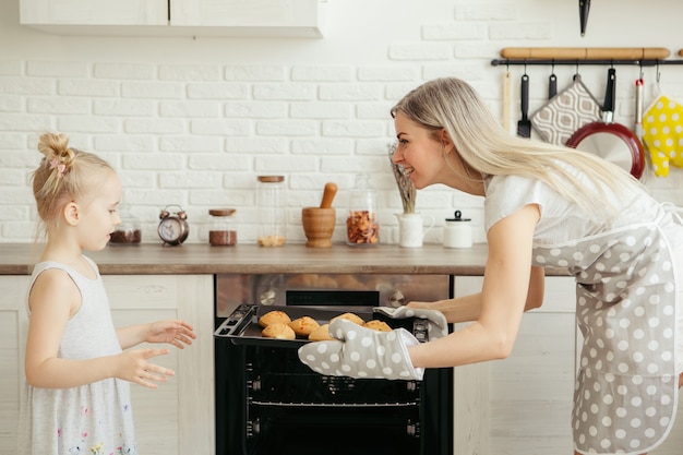 Niña linda ayuda a mamá a hornear galletas en la cocina. Familia feliz. Viraje.