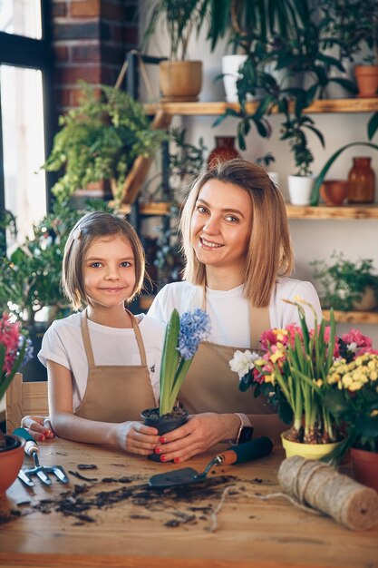 Niña linda ayuda a su madre a cuidar las plantas. Mamá y su hija se dedican a la jardinería. Familia feliz en primavera.