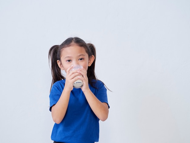 Niña linda bebiendo leche de vidrio a la luz