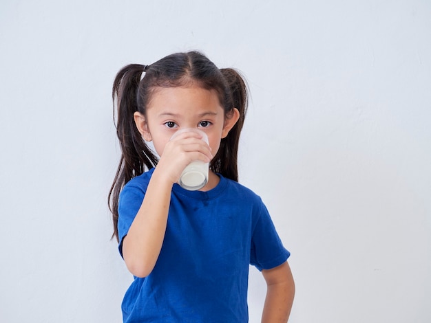 Niña linda bebiendo leche de vidrio a la luz