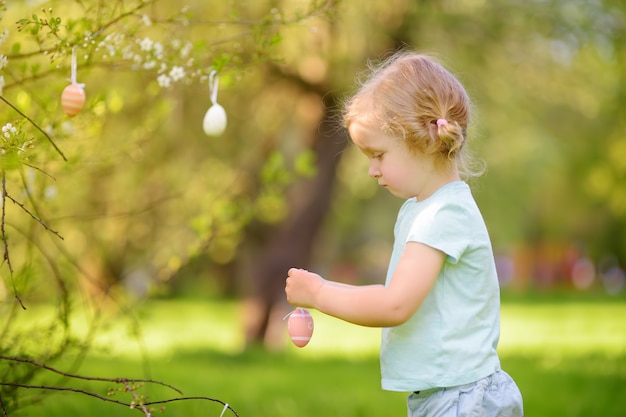 La niña linda busca el huevo de Pascua en el árbol floreciente de la rama.