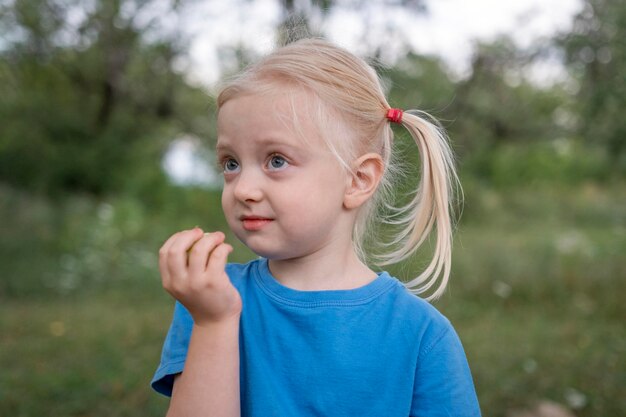 Niña linda con cabello rubio recogido en colas de caballo con manzana verde en la mano Niño en el jardín de verano pasa tiempo en la naturaleza