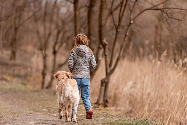 Niña linda caminando con perro golden retriever en primavera. vista desde atrás