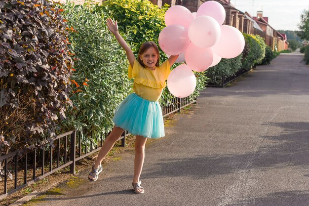 Niña linda en camisa amarilla y falda azul sonriendo y sosteniendo muchos globos