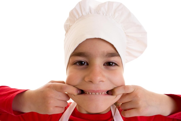 Niña linda con camisa roja con delantal blanco y sombrero de cocina blanco mostrando los dientes