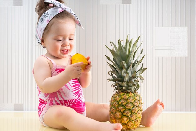 Niña linda en camisa rosa con estampado tropical sentada en la mesa y comiendo limón