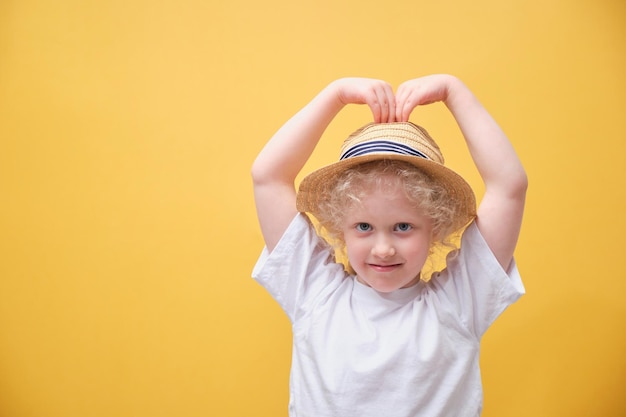 Niña linda con una camiseta blanca divirtiéndose con un niño con un sombrero de paja en un fondo amarillo