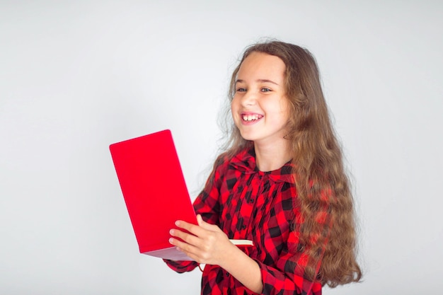 Niña linda con carpeta sonriendo de pie en la pared blanca, lugar para el texto, concepto de regreso a la escuela