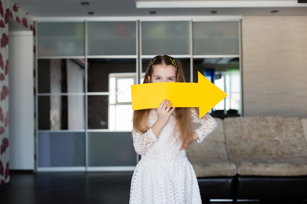 Niña linda con un cartel amarillo en blanco en la forma de una flecha que muestra a la derecha