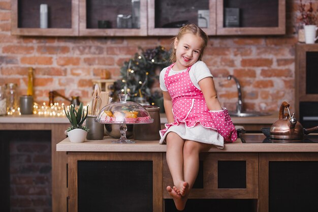 Niña linda en la cocina comiendo pastelitos