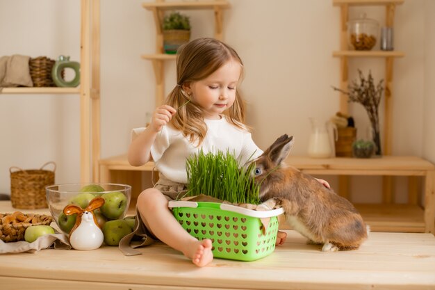 Niña linda en la cocina de madera de la casa alimenta la hierba fresca del conejo