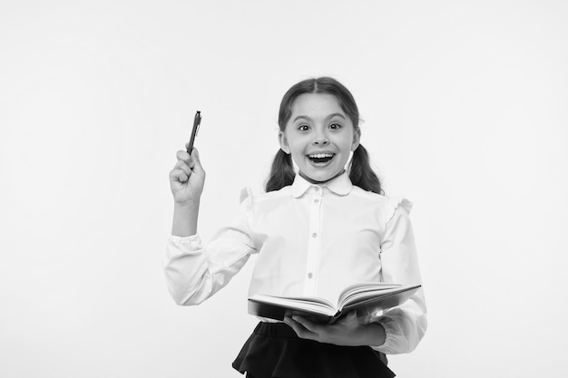 Niña linda colegiala en uniforme sostenga un libro o un libro de texto fondo amarillo Alumno diligente obtenga conocimiento del libro Niño use uniforme escolar prepárese para la lección su conocimiento Emocionado por el conocimiento