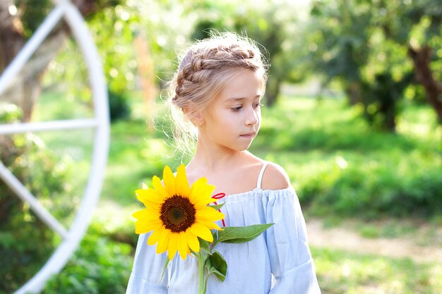 Niña linda con una coleta en la cabeza sostiene un girasol en el jardín de verano.