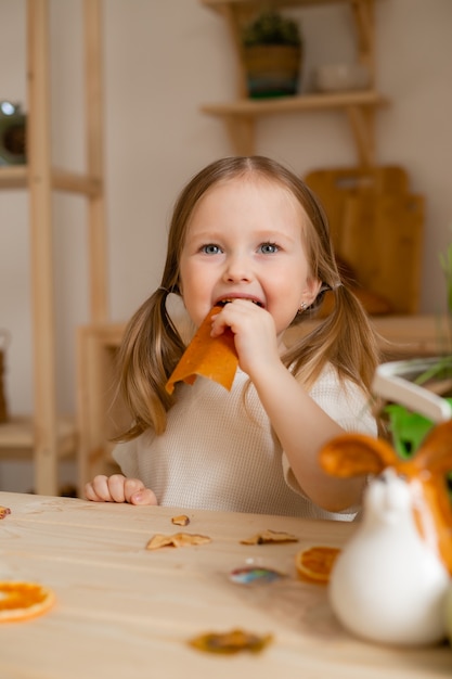 Niña linda come pastilla natural en casa en una cocina de madera.