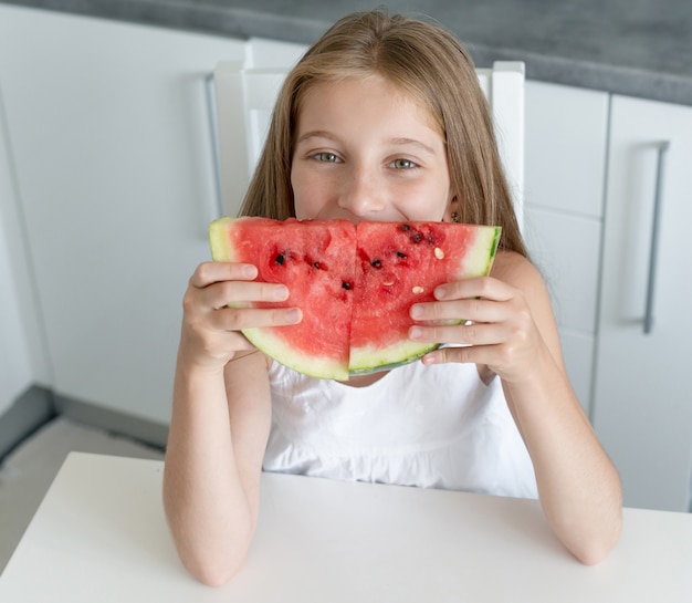 Niña linda come una sandía en la cocina