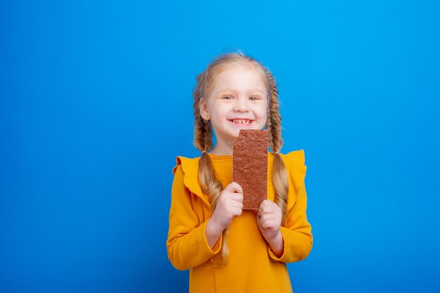 Niña linda comiendo chocolate en un fondo azul