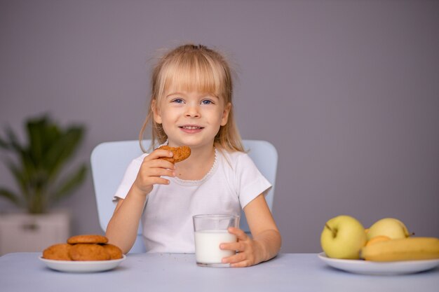 Niña linda comiendo galletas y bebiendo leche en casa o en el jardín de infantes