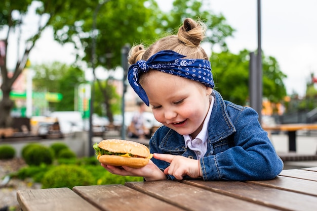 Foto niña linda comiendo una hamburguesa en un café. concepto de comida rápida para niños