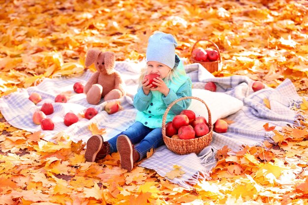 Niña linda comiendo manzanas rojas en el parque de otoño