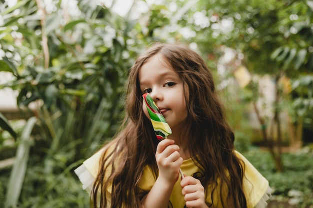 Niña linda comiendo una piruleta en forma de sandía Niño con piruletas en el jardín botánico