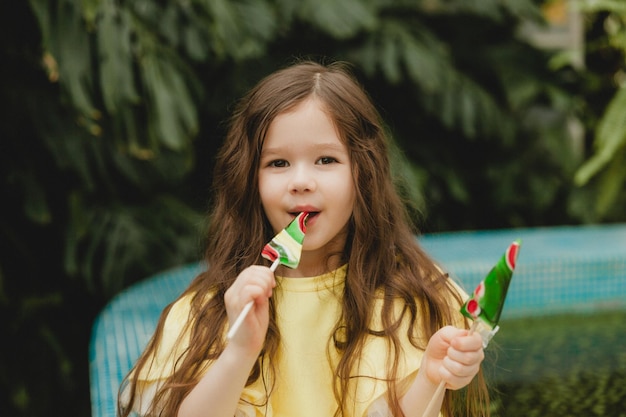 Niña linda comiendo una piruleta en forma de sandía Niño con piruletas en el jardín botánico