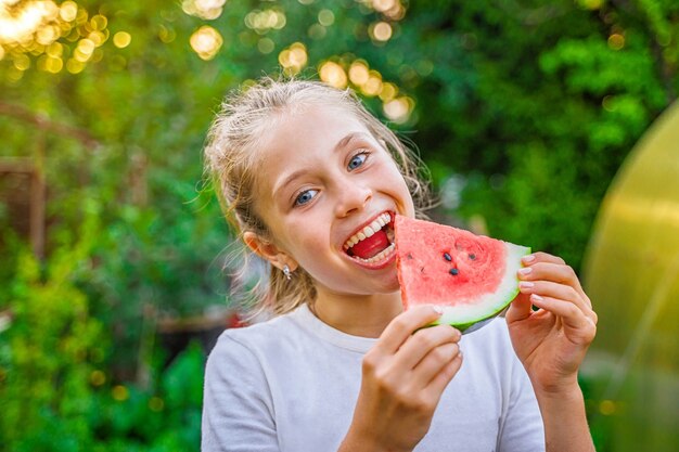 Niña linda comiendo sandía en el jardín verde