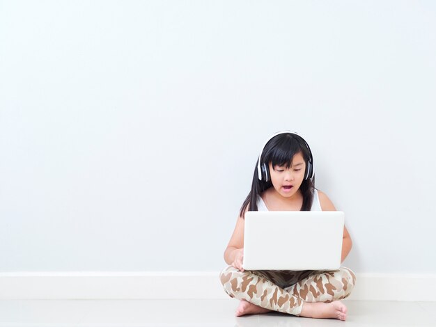 Niña linda con la computadora portátil en casa