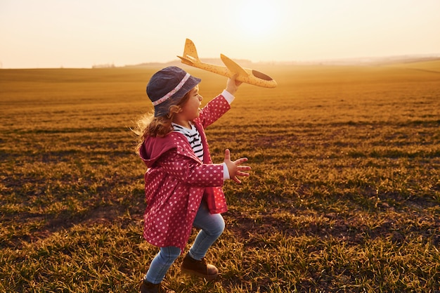 Niña linda corre con avión de juguete en el hermoso campo durante el día soleado